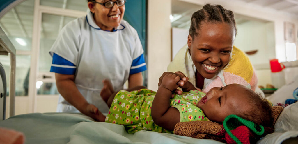 Baby with his mother at the hospital with nurse aide looking on